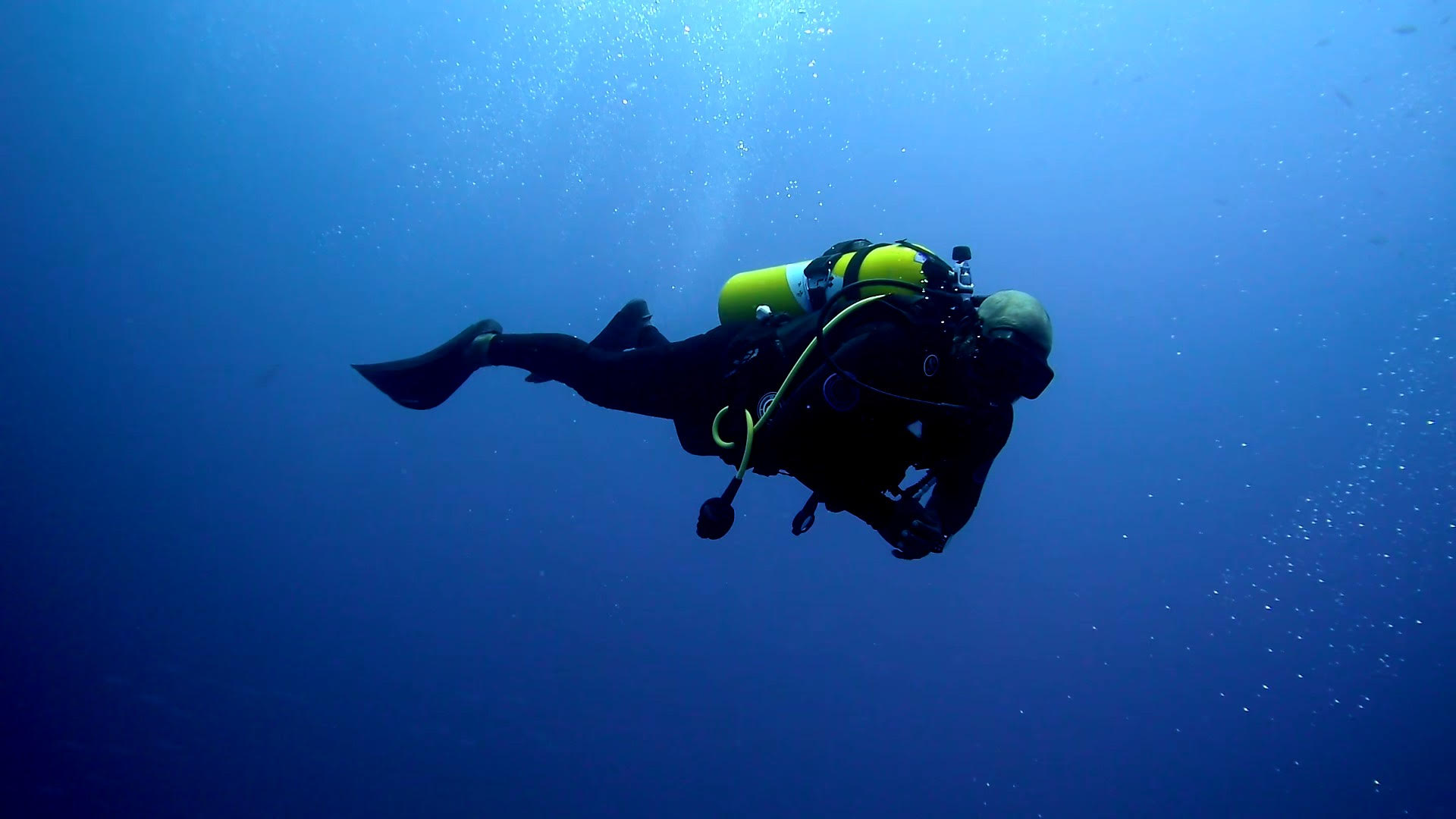 Scuba diver with a yellow air cylinder swimming through blue ocean water